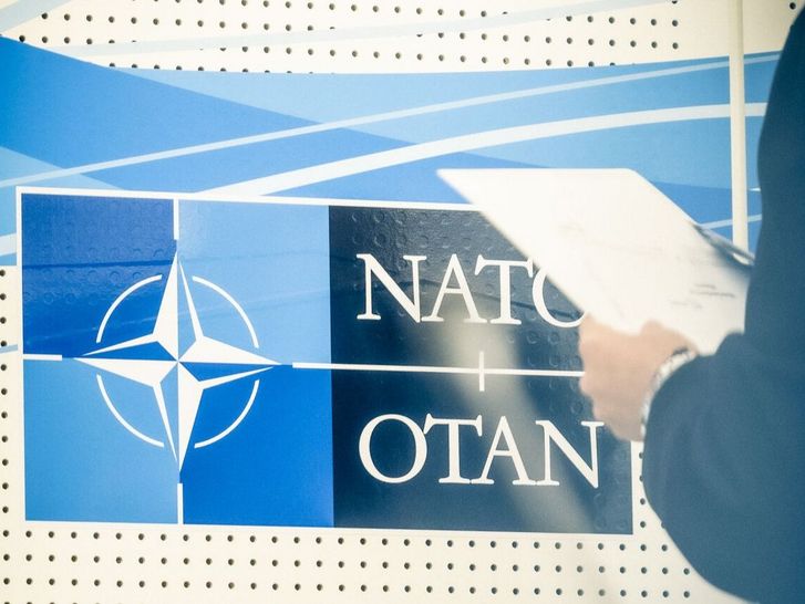 Eine Person mit Klemmbrett steht vor dem NATO-Logo